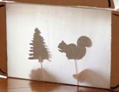 Silhouettes of a pine tree and a squirrel stick puppets with a silhouette of hands holding the puppets.