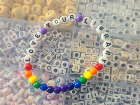 A bracelet with the text "Love your Library".  Bracelet has rainbow colored beads surrounding the phrase.