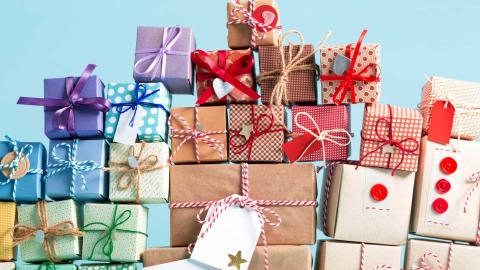 Piles of presents wrapped in a variety of different wrapping- blue, green, brown, white.  Some presents have bows.